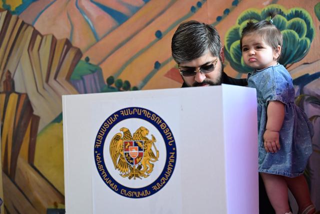 A man holding a child votes in Armenia's parliamentary election at a polling station in Yerevan on June 7, 2026. (Photo by Karen MINASYAN / AFP)