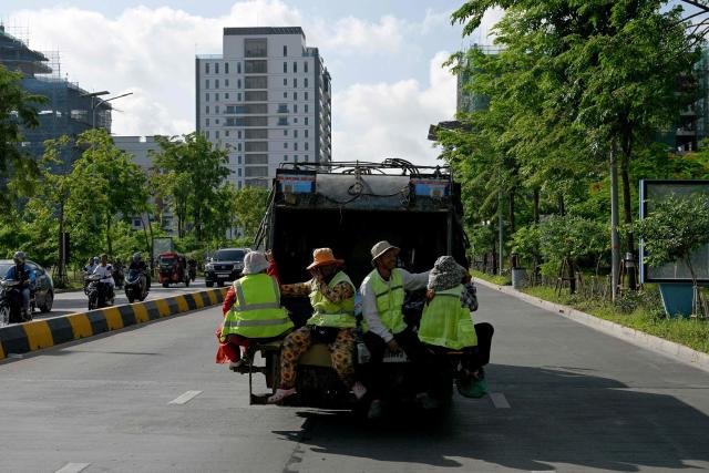 Workers ride at the back of a rubbish truck as they travel along a street in Phnom Penh on June 7, 2026. (Photo by TANG CHHIN Sothy / AFP)