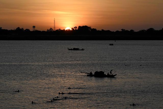 People swim near a fisherman's boat during sunrise over the Mekong River in Phnom Penh on June 7, 2026. (Photo by TANG CHHIN Sothy / AFP)