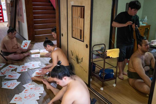 Sumo wrestlers organise signed sumo wrestler handprints for fans as another wrestler has his hair styled at the Dewanoumi sumo stable in Tokyo on June 4, 2026. The stable, founded in 1862 and one of the sport's oldest, has become a major lineage in modern sumo, producing many top-division wrestlers. (Photo by Andrew CABALLERO-REYNOLDS / AFP)