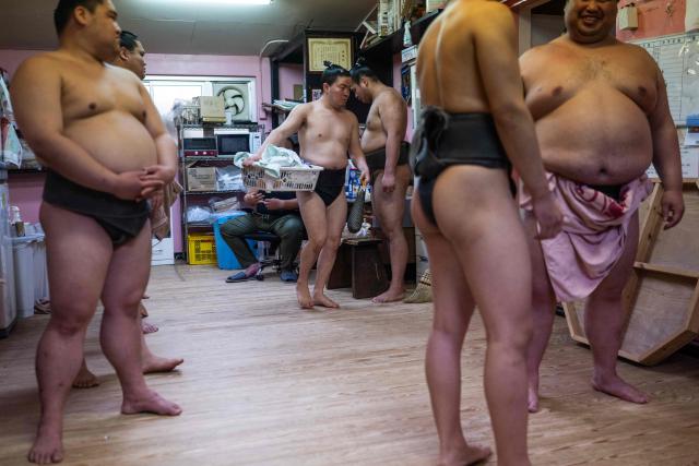 A sumo wrestler carries his laundry as others wait to have lunch at the Dewanoumi sumo stable in Tokyo on June 4, 2026. The stable, founded in 1862 and one of the sport's oldest, has become a major lineage in modern sumo, producing many top-division wrestlers. (Photo by Andrew CABALLERO-REYNOLDS / AFP)