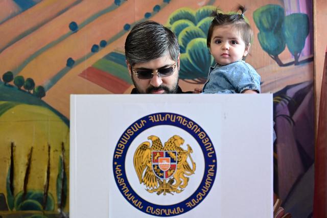 A man holding a child votes in Armenia's parliamentary election at a polling station in Yerevan on June 7, 2026. (Photo by Karen MINASYAN / AFP)