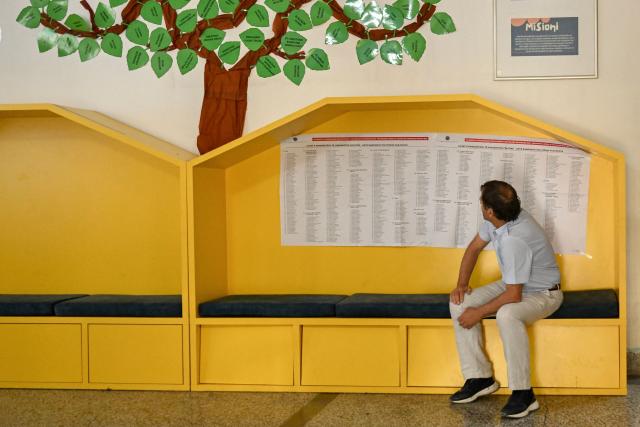 A man sits next to lists of political candidate displayed at a polling station on the day of general elections in Pristina on June 7, 2026. Polls opened on June 7, 2026 for another snap election in Kosovo, its third in just over a year, as voter frustration mounts at a grinding political gridlock in Europe's youngest country, as the ballot comes after a polarised parliament failed to elect a president in April, deepening a political crisis that has gripped the country since inconclusive parliamentary elections in February 2025. (Photo by Armend NIMANI / AFP)