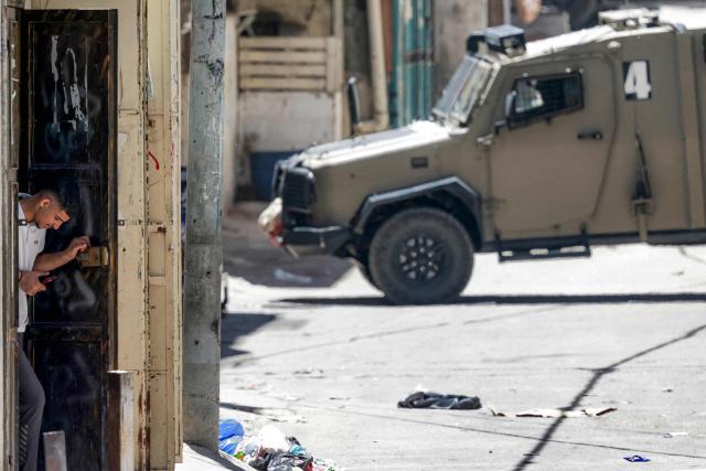 A man takes cover as Israeli army armoured vehicles move along alleys in the Balata camp for Palestinian refugees, east of Nablus in the occupied West Bank, during a military operation on June 7, 2026. Since the war in Gaza broke out in October 2023 with Hamas's attack on Israel, near-daily violence has rocked the West Bank, which Israel has occupied since 1967. Israeli soldiers or settlers have killed at least 1,080 Palestinians since then, including both militants and civilians, according to an AFP tally based on Palestinian health ministry data. (Photo by Jaafar ASHTIYEH / AFP)