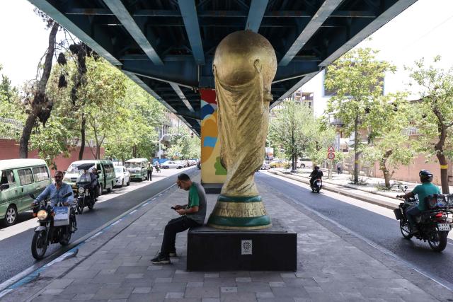 An Iranian man sits beneath a World Cup trophy displayed under a bridge in Tehran on June 7, 2026. Iran's national team, also known as Team Melli, open their 2026 World Cup campaign, co-hosted by the United States, Mexico and Canada, against New Zealand in Los Angeles on June 15 before lining up against Belgium and Egypt in Group G. Iran has been at war with the United States and Israel since February 28, though a fragile ceasefire has been in place since April 8. Tehran and Washington have had no diplomatic relations since 1980 following the hostage crisis at the US embassy, which came after the Islamic revolution that toppled the US-backed shah. (Photo by ATTA KENARE / AFP)