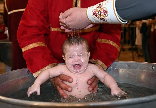 A Georgian Orthodox priest baptises a child during a mass baptism ceremony at the Sameba Cathedral in Tbilisi on June 7, 2026. (Photo by Vano SHLAMOV / AFP)
