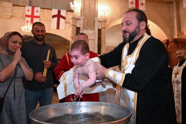 A Georgian Orthodox priest baptises a child during a mass baptism ceremony at the Sameba Cathedral in Tbilisi on June 7, 2026. (Photo by Vano SHLAMOV / AFP)