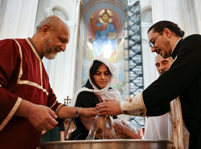 A Georgian Orthodox priest baptises a child during a mass baptism ceremony at the Sameba Cathedral in Tbilisi on June 7, 2026. (Photo by Vano SHLAMOV / AFP)