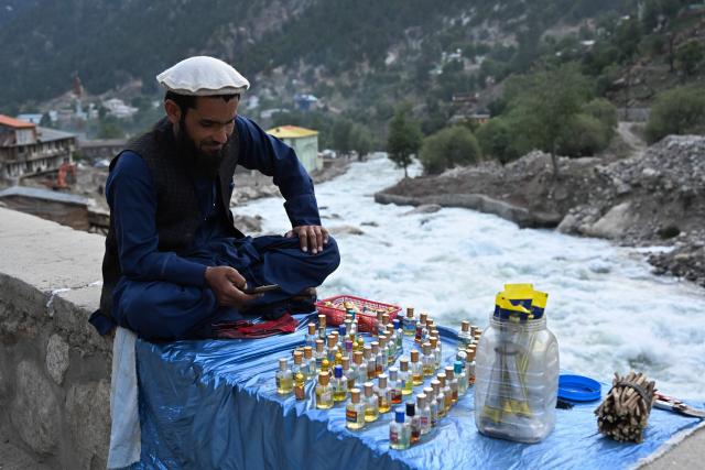 An Afghan perfume vendor uses his phone as he waits for customers along a riverside at Parun in Nuristan province on June 7, 2026. (Photo by Wakil KOHSAR / AFP)