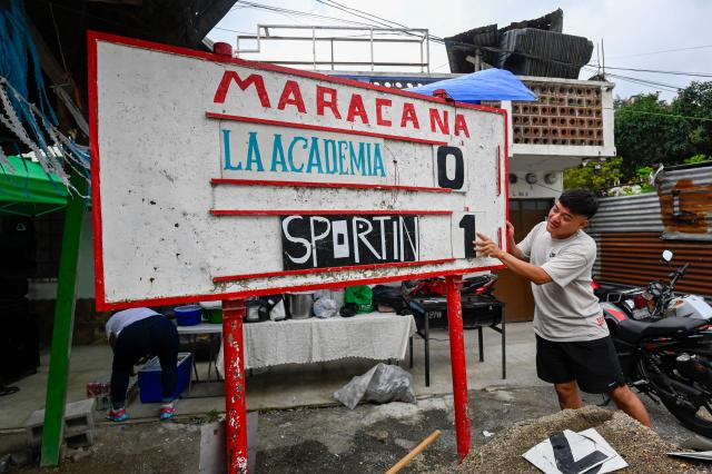 A man adjusts the scoreboard during an amateur football match between "La Academia" and "Sportin" at the Maracana pitch in La Limonada neighbourhood in Guatemala City on June 7, 2026. Named after the iconic Maracana Stadium in Brazil, these dirt fields of the same name are a landmark of amateur football in Guatemala City. The Maracana pitch is located in an area that for years was marked by violence, bringing together players and fans from different neighborhoods of the capital every week. (Photo by Johan ORDONEZ / AFP)