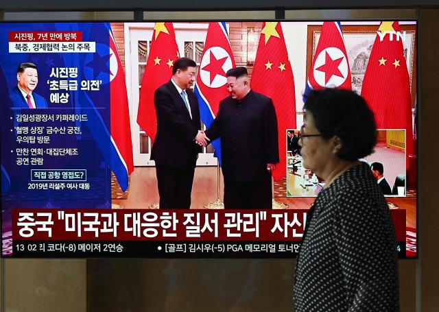 A woman walks past a television screen showing a news broadcast with file footage of the 2019 meeting between China's President Xi Jinping and North Korean leader Kim Jong Un, at a train station in Seoul on June 8, 2026. China's President Xi Jinping hailed an "invincible friendship" with Pyongyang as he arrived in North Korea on June 8, his first trip abroad this year after hosting back-to-back summits in Beijing. (Photo by Jung Yeon-je / AFP)