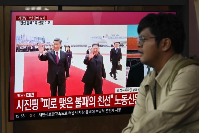 A man walks past a television screen showing a news broadcast with file footage of the 2019 meeting between China's President Xi Jinping and North Korean leader Kim Jong Un, at a train station in Seoul on June 8, 2026. China's President Xi Jinping hailed an "invincible friendship" with Pyongyang as he arrived in North Korea on June 8, his first trip abroad this year after hosting back-to-back summits in Beijing. (Photo by Jung Yeon-je / AFP)