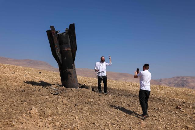 A man poses for a photos next to a fallen rock half-buried in the ground on the outskirts of Jericho on June 8, 2026, following Iranian and Iran-backed Houthi rebel attacks. Israel and Iran traded fire on June 8, seriously testing a fragile truce and threating hopes for a deal to end the Middle East war. (Photo by AHMAD GHARABLI / AFP) / 