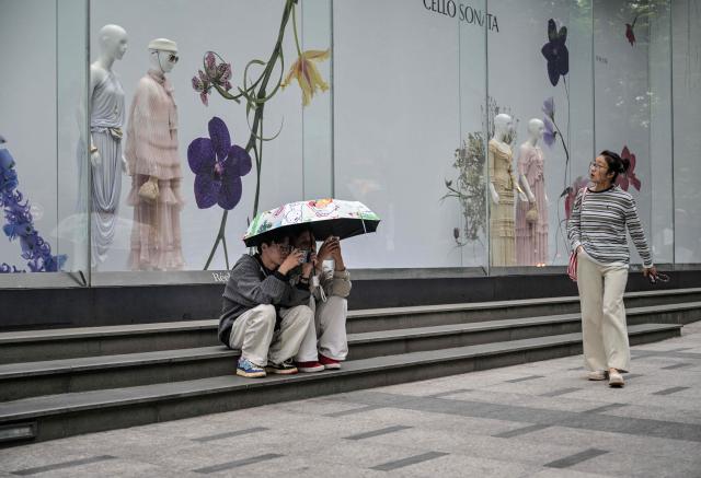 People are seen on a street next to a shop in the Jing' an district of Shanghai on June 8, 2026. (Photo by HECTOR RETAMAL / AFP)