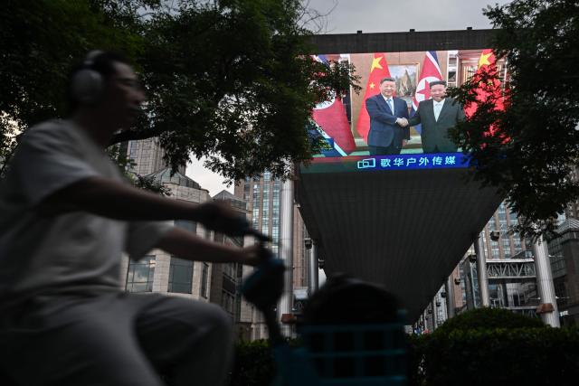 A man rides past a giant screen displayed outside a shopping mall in Beijing on June 8, 2026, showing a news program about the meeting between China's President Xi Jinping and North Korean leader Kim Jong Un held in North Korea. China's President Xi Jinping made a rare visit to North Korea on June 8, where he proclaimed a willingness to bring ties to "new heights" during a meeting with Kim Jong Un. (Photo by Pedro PARDO / AFP)