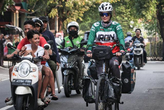 Iranian cyclist Arezoo Eskandari (R), 35, who is traveling across Asia, rides her bicycle on a street in Jakarta on June 8, 2026. Eskandari has cycled thousands of kilometers across Asia, aiming to promote peace, friendship and cultural understanding. (Photo by Aditya Irawan / AFP)