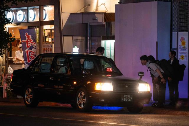 People bow to a colleague entering a taxi after leaving a bar in Tokyo on June 8, 2026. (Photo by Andrew CABALLERO-REYNOLDS / AFP)