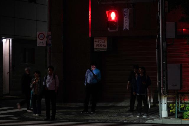 A man (C) looks at his phone as he waits to cross the street in Tokyo's Ginza district on June 8, 2026. (Photo by Andrew CABALLERO-REYNOLDS / AFP)