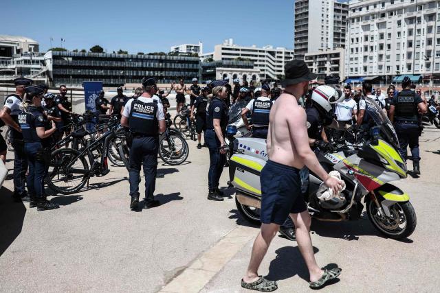 A beach goer walks past police officers gathering along the promenade in Catalans beach during a media briefing on security measures implemented on Marseille’s beaches, in southeastern France, on June 8, 2026. (Photo by Thibaud MORITZ / AFP)