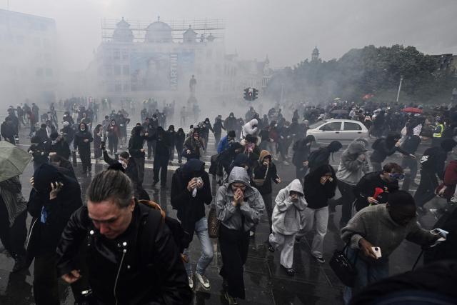Protesters reacts to tear gas launched by police officers during a demonstration against police brutality that occurred during past rallies organised to protest against austerity measures affecting the education sector, in central Brussels, on June 8, 2026. (Photo by ERIC LALMAND / Belga / AFP) / Belgium OUT