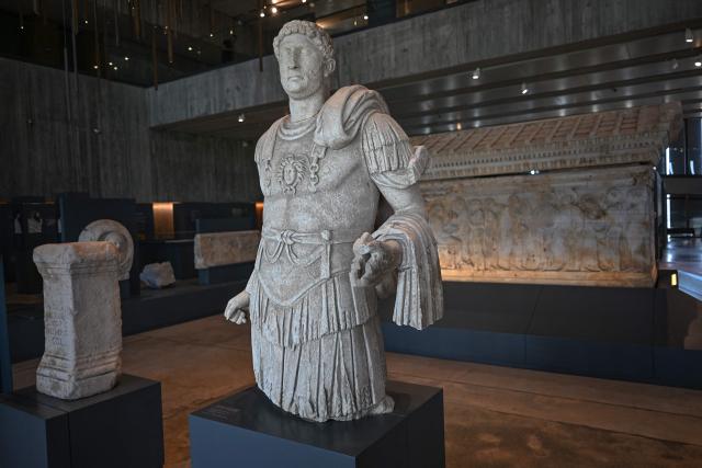 The statue of Roman emperor Hadrian (front) and the tomb of Polyksena (back), found at  excavation sites, are displayed at the Troy museum in Canakkale on June 2,2026. A gift from the film set of "Troy", the giant Trojan Horse replica looms over the port of Canakkale on the Dardanelles Strait in western Turkey. First related by Homer, then retold for the silver screen in 2004, with Brad Pitt as Achilles, the legend of the ancient city travels to Rome's Colosseum this week, where a major new exhibition opens on June 12, 2026. (Photo by Ozan KOSE / AFP)