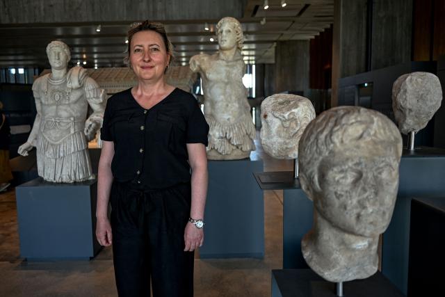 Troy Museum director Sinem Duzgoren poses in front of statues found at excavation sites at the Troy Museum in Canakkale on June 2, 2026. A gift from the film set of "Troy", the giant Trojan Horse replica looms over the port of Canakkale on the Dardanelles Strait in western Turkey. First related by Homer, then retold for the silver screen in 2004, with Brad Pitt as Achilles, the legend of the ancient city travels to Rome's Colosseum this week, where a major new exhibition opens on June 12, 2026. (Photo by Ozan KOSE / AFP)