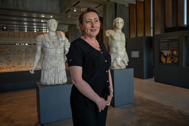 Troy Museum director Sinem Duzgoren poses in front of statues found at excavation sites at the Troy Museum in Canakkale on June 2, 2026. A gift from the film set of "Troy", the giant Trojan Horse replica looms over the port of Canakkale on the Dardanelles Strait in western Turkey. First related by Homer, then retold for the silver screen in 2004, with Brad Pitt as Achilles, the legend of the ancient city travels to Rome's Colosseum this week, where a major new exhibition opens on June 12, 2026. (Photo by Ozan KOSE / AFP)