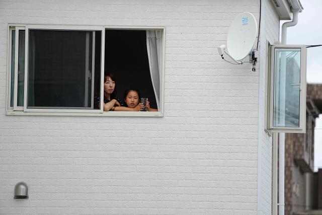 Residents look out from a home as hunters and zoo staff search for a wild bear in Utsunomiya, north of Tokyo, on June 9, 2026. A bear roaming the streets of a Japanese city for days forced the closure of nearly 100 schools, as dozens of hunters and officials searched for the animal. (Photo by Yuichi YAMAZAKI / AFP)