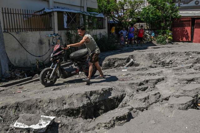 A man pushes a motorcycle along a damaged road after a 7.8 magnitude earthquake in General Santos City on June 9, 2026. A 7.8-magnitude earthquake in the southern Philippines on June 8 killed at least 35 people, according to provincial authorities, after toppling buildings and sparking tsunami warnings across the region. (Photo by Jam STA ROSA / AFP)