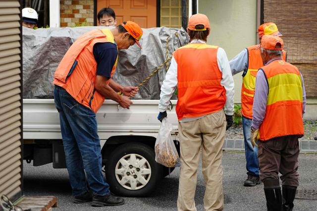 Hunters stand next to a truck carrying a sedated wild bear after it was captured in Utsunomiya, north of Tokyo, on June 9, 2026. A bear roaming the streets of a Japanese city for days forced the closure of nearly 100 schools, as dozens of hunters and officials searched for the animal. (Photo by Yuichi YAMAZAKI / AFP)