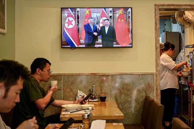 People eat at a restaurant in Shanghai next to a screen showing a news program about the meeting between Chinese President Xi Jinping and North Korean leader Kim Jong Un in Pyongyang, on June 9, 2026. China's President Xi Jinping made a rare visit to North Korea on June 8, where he proclaimed a willingness to bring ties to "new heights" during a meeting with Kim Jong Un. (Photo by Jade GAO / AFP)