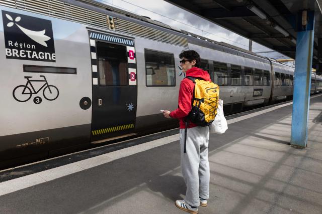 A passenger stands on a train platform next to a Region Bretagne regional train at a railway station in Quimper, western France, June 9, 2026. One in three TGV trains and one in two Intercitйs trains will remain in station on June 10, 2026, and regional traffic will be “severely disrupted” as the four representative unions at SNCF are calling for a 24-hour strike on June 10, 2026, to demand a moratorium on the arrival of competition on the market, the first social test of the Castex era. (Photo by Fred TANNEAU / AFP)