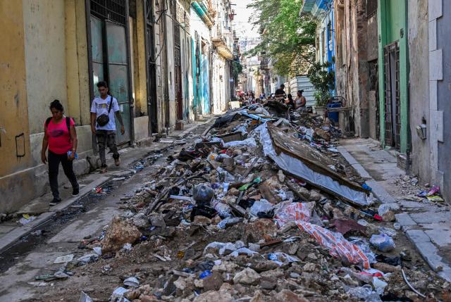 People walk past piled-up rubbish in a street in Havana on June 9, 2026. (Photo by YAMIL LAGE / AFP)