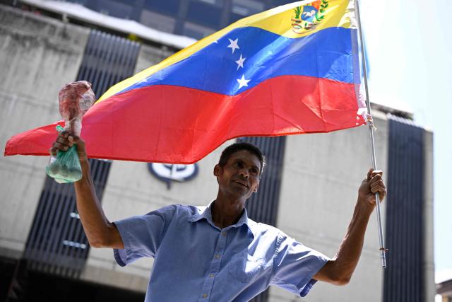 A man waves a Venezuelan national flag as he holds up a cow bone during a protest demanding better working conditions and presidential elections, outside the Public Prosecutor's Office in Caracas on June 9, 2026. (Photo by Maxwell BRICENO / AFP)