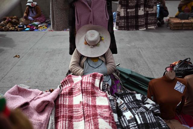 A woman naps while selling clothes at an improvised market along a blocked highway in the Rio Seco area of El Alto, Bolivia, on June 9, 2026. The road, a key transport corridor linking La Paz with Copacabana and the border town of Desaguadero, has been transformed into a bustling marketplace where hundreds of vendors sell food and other goods as anti-government road blockades continue across the country amid growing political tensions and supply shortages. (Photo by Marvin RECINOS / AFP)