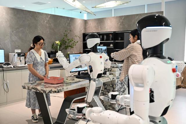 An engineer trains a humanoid robot to do household tasks at the X Square Robot facilities in Shenzhen, southern China's Guangdong province on May 22, 2026. China's robots have wowed audiences with fluid dancing and set-piece martial arts displays onstage, but their application and performance in real-life settings remains limited. For companies like X Square, the logic of launching an imperfect service lies in data collection for so-called embodied artificial intelligence. (Photo by Hector RETAMAL / AFP) / To go with AFP story China-tech-labour-lifestyle-AI, FOCUS by Emily WANG