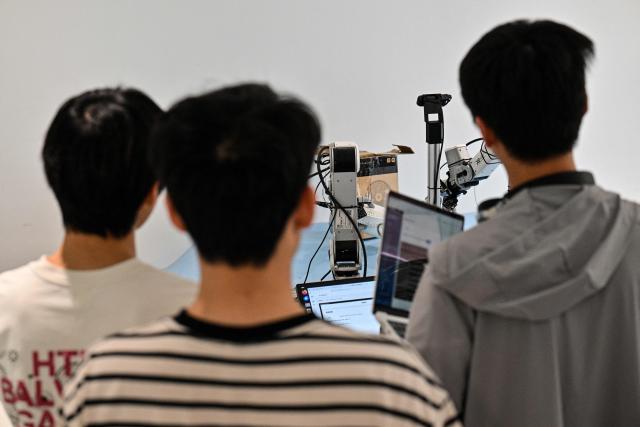 Engineers train a humanoid robot to do household tasks at the X Square Robot facilities in Shenzhen, southern China's Guangdong province on May 22, 2026. China's robots have wowed audiences with fluid dancing and set-piece martial arts displays onstage, but their application and performance in real-life settings remains limited. For companies like X Square, the logic of launching an imperfect service lies in data collection for so-called embodied artificial intelligence. (Photo by Hector RETAMAL / AFP) / To go with AFP story China-tech-labour-lifestyle-AI, FOCUS by Emily WANG