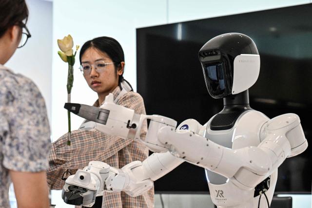 An engineer trains a humanoid robot to do household tasks at the X Square Robot facilities in Shenzhen, southern China's Guangdong province on May 22, 2026. China's robots have wowed audiences with fluid dancing and set-piece martial arts displays onstage, but their application and performance in real-life settings remains limited. For companies like X Square, the logic of launching an imperfect service lies in data collection for so-called embodied artificial intelligence. (Photo by Hector RETAMAL / AFP) / To go with AFP story China-tech-labour-lifestyle-AI, FOCUS by Emily WANG