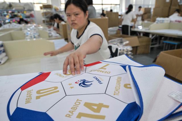 In this photo taken on June 5, 2026 a worker packs merchandise of France's football team, which will participate in the FIFA World Cup 2026, at the All Star Partner factory in Yiwu in eastern China's Zhejiang province. Stuffed "goat" plushies donning Lionel Messi's famous Argentina no. 10 pepper a factory tabletop in eastern China, where sellers are betting on the country's lucrative fan market for a World Cup boost. (Photo by Hector RETAMAL / AFP) / To go with 'CHINA-CONSUMPTION-FBL,FOCUS' by Mary YANG