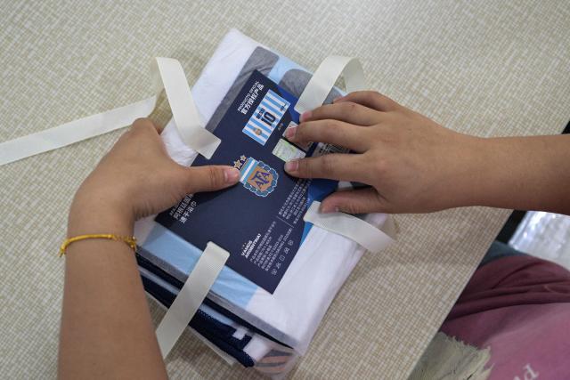 In this photo taken on June 5, 2026 a worker packs merchandise of Argentina's football team, which will participate in the FIFA World Cup 2026, at the All Star Partner factory in Yiwu in eastern China's Zhejiang province. Stuffed "goat" plushies donning Lionel Messi's famous Argentina no. 10 pepper a factory tabletop in eastern China, where sellers are betting on the country's lucrative fan market for a World Cup boost. (Photo by Hector RETAMAL / AFP) / To go with 'CHINA-CONSUMPTION-FBL,FOCUS' by Mary YANG