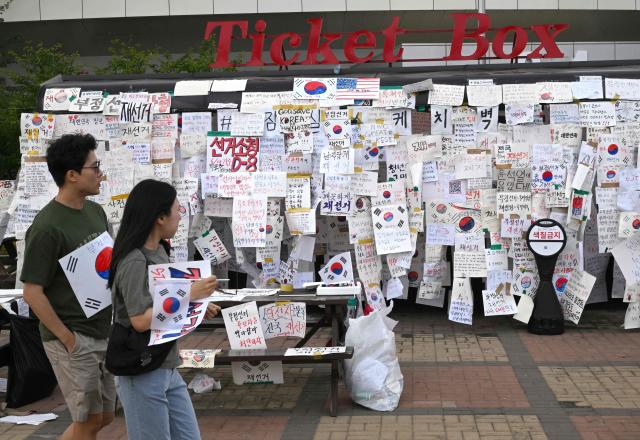 South Korean protesters walk past messages calling for a rerun of the local elections due to a shortage of ballot papers outside a vote-counting centre in Seoul on June 10, 2026. South Korean authorities agreed on June 9 to launch an investigation into ballot paper shortages at recent local elections, local media reported, following widespread protests. (Photo by Jung Yeon-je / AFP)
