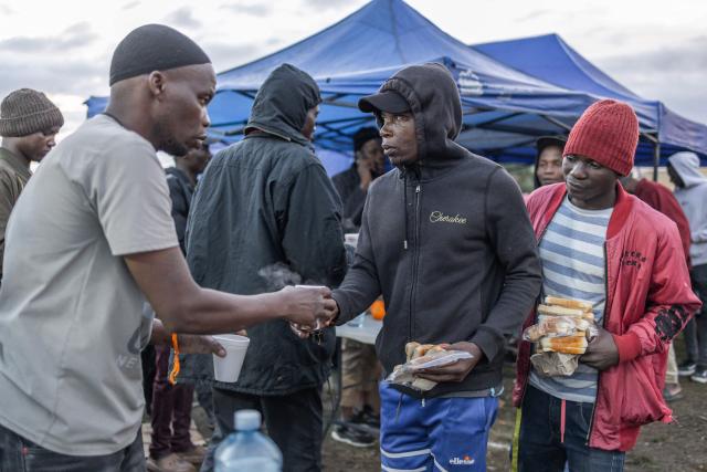 A volunteer hands out a cup of tea to a displaced foreign national taking refuge with others in a park in Durban on June 10, 2026 after fleeing their homes amid fears of xenophobic attacks. Hundreds of foreign nationals await repatriation to Malawi from South Africa following xenophobic violence in the country. Foreign nationals have told of intimidation and beatings by mobs going door-to-door to tell them to leave by June 30, a "deadline" regularly broadcast across social media, even though it has no official backing. Ghana, Mozambique and Malawi are among countries that have repatriated hundreds of their nationals this month, most of whom South Africa says did not have the correct documentation to be in the country. (Photo by RAJESH JANTILAL / AFP)