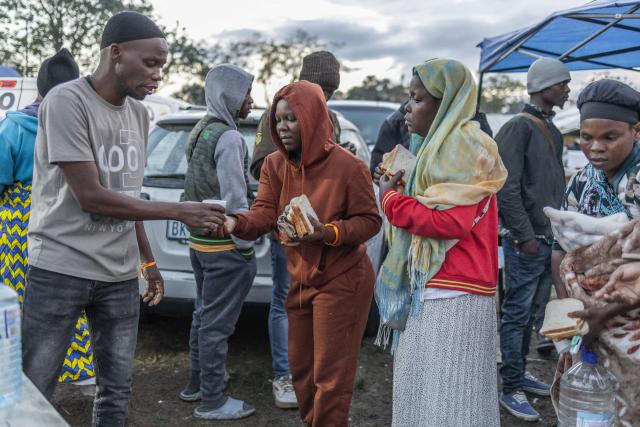A volunteer hands out a cup of tea to a displaced foreign national taking refuge with others in a park in Durban on June 10, 2026 after fleeing their homes amid fears of xenophobic attacks. Hundreds of foreign nationals await repatriation to Malawi from South Africa following xenophobic violence in the country. Foreign nationals have told of intimidation and beatings by mobs going door-to-door to tell them to leave by June 30, a "deadline" regularly broadcast across social media, even though it has no official backing. Ghana, Mozambique and Malawi are among countries that have repatriated hundreds of their nationals this month, most of whom South Africa says did not have the correct documentation to be in the country. (Photo by RAJESH JANTILAL / AFP)