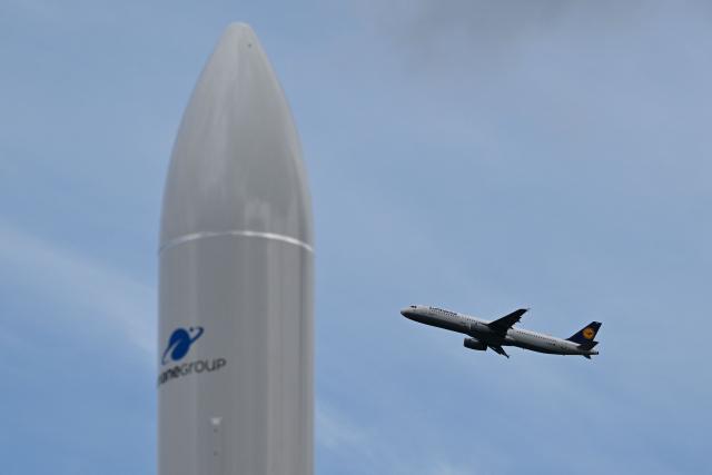 An airplane Airbus A321 of Lufthansa (R) flies upwards in the sky after take off as a replica of an ESA Ariane rocket stands on the ground of the International Aerospace Exhibition (ILA) on its opening day in Schoenefeld, near Berlin on June 10, 2026. (Photo by RALF HIRSCHBERGER / AFP)