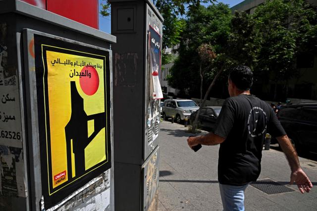 A man walks past a placard pasted on an electricity booth in Beirut on June 10, 2026, depicting the logo of Hezbollah military media with Arabic wording that reads 'Days, nights and the field between us'. Iran has insisted any deal to end the war must include a truce in Lebanon, which was drawn into the conflict when Iran-backed Hezbollah militants within its borders fired rockets at Israel on March 2. (Photo by Joseph EID / AFP)