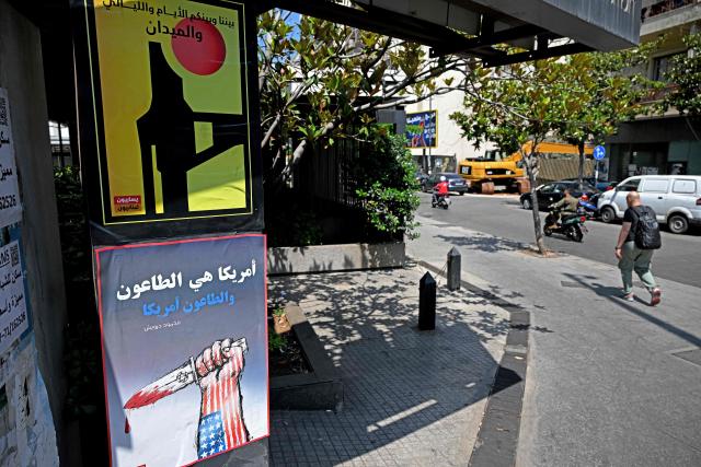 A man walks past placards pasted on an electricity booth in Beirut on June 10, 2026, depicting (top) the logo of Hezbollah military media with Arabic wording that reads 'Days, nights and the field between us' and (bottom) 'The plague is America and America is the stabber in America'. Iran has insisted any deal to end the war must include a truce in Lebanon, which was drawn into the conflict when Iran-backed Hezbollah militants within its borders fired rockets at Israel on March 2. (Photo by Joseph EID / AFP)