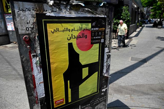 A man walks past a placard pasted on an electricity booth in Beirut on June 10, 2026, depicting the logo of Hezbollah military media with Arabic wording that reads 'Days, nights and the field between us'. Iran has insisted any deal to end the war must include a truce in Lebanon, which was drawn into the conflict when Iran-backed Hezbollah militants within its borders fired rockets at Israel on March 2. (Photo by Joseph EID / AFP)