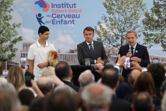 Adrien Taquet (R), Chairman of the Supervisory Board of the Robert-Debre Institute for the Child's Brain, delivers a speech as French President Emmanuel Macron (C) and a patient Joshua Krieff listen during the foundation stone laying ceremony for the Child Brain Institute (ICE - Institut Robert-Debre du Cerveau de l’Enfant) at the Robert-Debre Hospital in Paris on June 10, 2026. (Photo by Gonzalo Fuentes / POOL / AFP)