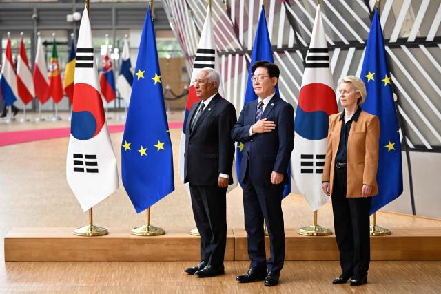 European Union (EU) Council President Antonio Costa (L) and European Commission President Ursula von der Leyen (R) stand with South Korean President Lee Jae Myung (C) as they listen to anthems upon arrival for an EU-Korea Summit in Brussels on June 10, 2026. (Photo by Nicolas TUCAT / AFP)