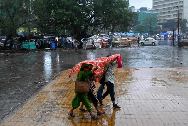 Pedestrians walk across a water-logged street during raifall in Kolkata on June 10, 2026. (Photo by Dibyangshu SARKAR / AFP)